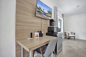Ein modernes Hotelzimmer mit Schreibtisch aus Holz, einem flachbildfernseher an der Wand, einer eingebauten Mikrowelle und einer Sitzecke mit Stuhl und Sofa.
