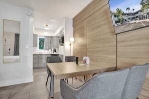 Ein modernes Hotelzimmer mit einer Wand aus Holzpaneelen, einem Essbereich mit Tisch und Stühlen, einer Küche im Hintergrund und Blick auf das Hotelgebäude.