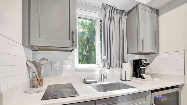 A modern kitchen with grey cabinets, a built-in oven, a sink, and a window with curtains.