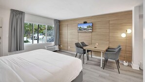 Ein Hotelzimmer mit Bett, Schreibtisch mit zwei Stühlen, Wandfernseher und großem Fenster mit Vorhängen.