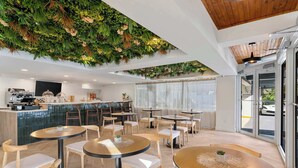 Ein modernes Café mit runden Tischen, Holzstühlen, einer Bar und einer Wanddekoration in Grün.