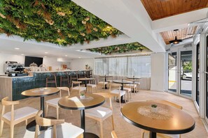 Ein modernes Café mit runden Tischen, Holzstühlen, einer Bar und einer Wanddekoration in Grün.