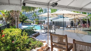 Ein Poolbereich im Freien mit Liegestühlen, Sonnenschirmen und einem Restaurant namens 'The Greenhouse Terrace Pool Bar'.
