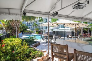 Ein Poolbereich im Freien mit Liegestühlen, Sonnenschirmen und einem Restaurant namens 'The Greenhouse Terrace Pool Bar'.