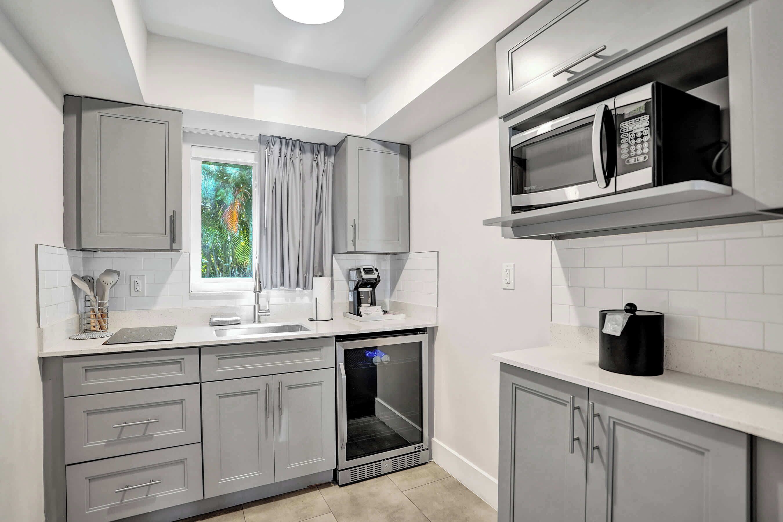 A compact kitchen with grey cabinets, a built-in microwave, a coffee machine, and a small refrigerator.