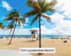 A beach scene with palm trees, a lifeguard tower, and beach umbrellas. - Coastal King Suite Stay at Ocean Blvd (Fort Lauderdale)