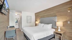 Quarto de hotel moderno com uma cama grande, mesas de cabeceira com luminárias, uma escrivaninha com cadeira e uma televisão fixada na parede.