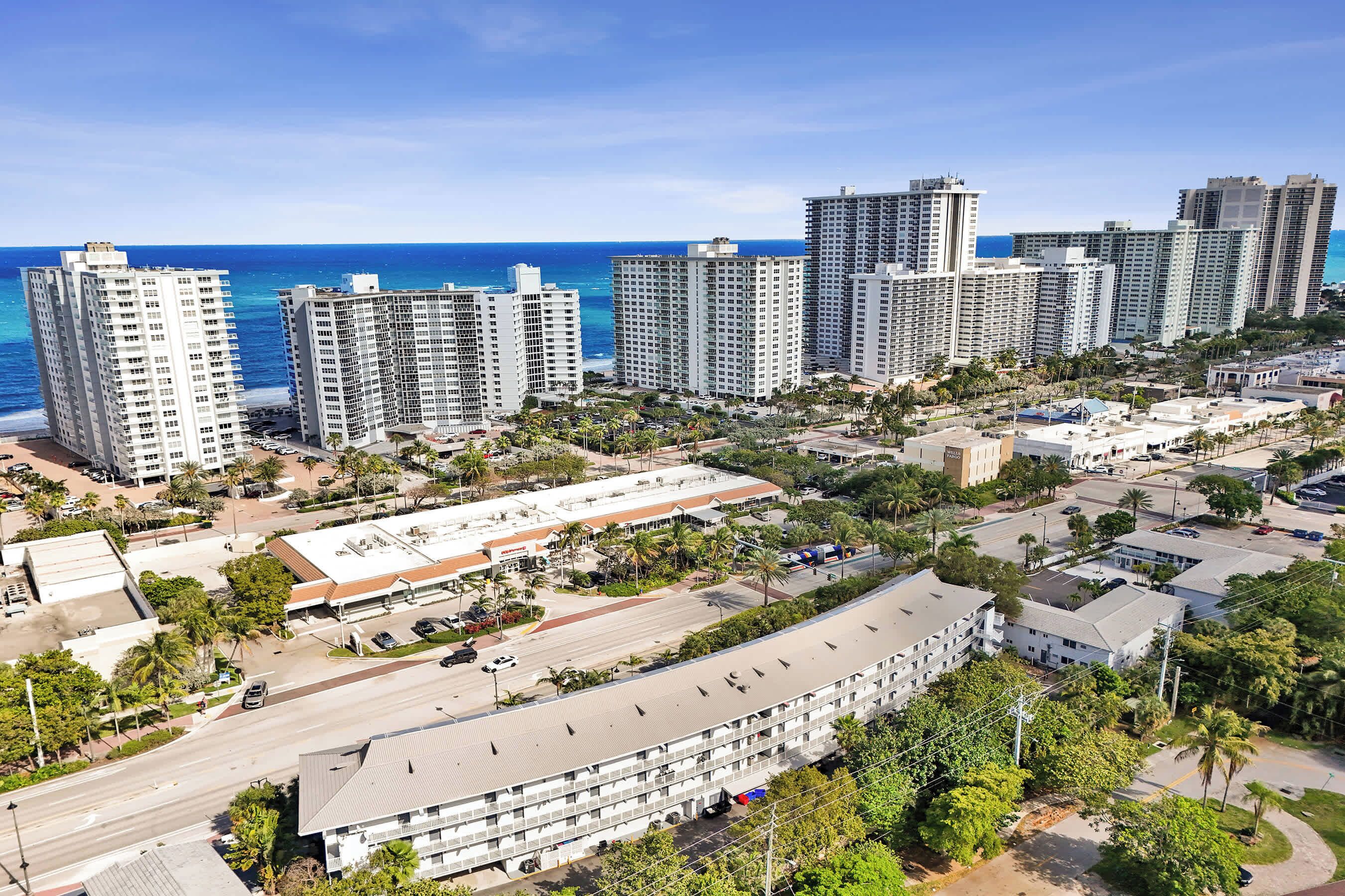 A high-rise hotel with multiple floors, a parking lot, and a view of the ocean.