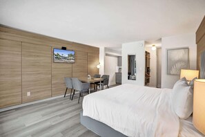 Ein modernes Hotelzimmer mit einem großen Bett, einem Schreibtisch mit Stühlen, einem an der Wand befestigten Fernseher und Blick ins Freie.