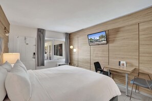 Ein Hotelzimmer mit Bett, Schreibtisch, Stuhl, Fernseher und Fenster.