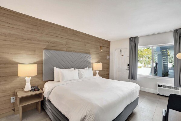 Une chambre d’hôtel avec un grand lit, deux tables de chevet avec des lampes, une fenêtre avec des rideaux et une vue sur les bâtiments environnants.