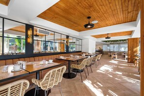 Un café moderno con vigas de madera en el techo, amplias ventanas y mobiliario de mimbre.