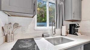 A modern kitchen with a built-in stove, a sink, and a window with curtains. - Boutique King Suite w/ Kitchenette (Fort Lauderdale)