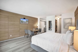 A modern hotel room with a large bed, a desk with chairs, a TV mounted on the wall, and a view of the outside. - Boutique King Suite w/ Kitchenette (Fort Lauderdale)