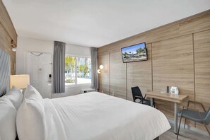 Ein Hotelzimmer mit Bett, Schreibtisch, Sessel, Fernseher und einem Fenster mit Vorhängen.