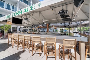 Ein Außenbereich mit Bar, ausgestattet mit Korbstühlen und einer Theke, unter einer Markise mit dem Schriftzug 'THE TERRACE'.