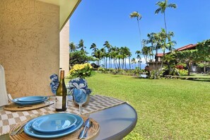 Ein Tisch draußen mit Flasche und Glas, Palmen und Blick auf das Meer.