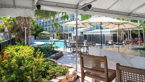 Un espace piscine extérieur doté de chaises longues, de parasols et d’un restaurant appelé « The Greenhouse Terrace Pool Bar ».
