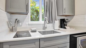 Une cuisine moderne avec des meubles gris, un évier, une fenêtre donnant sur des arbres et une machine à café.