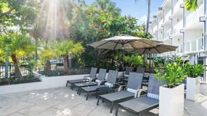 Une terrasse avec des chaises longues, un grand parasol et des plantes en pot.