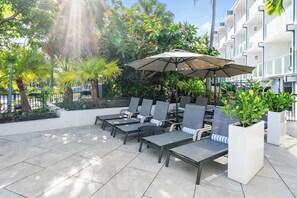 A patio with lounge chairs, a large umbrella, and potted plants. - Beachside Two Double Suite with Kitchenette (Fort Lauderdale)