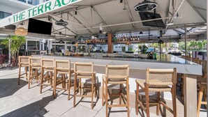 Uma área de bar ao ar livre com cadeiras de vime e um balcão, sob uma marquise com a inscrição 'THE TERRACE'.
