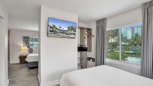 Een hotelkamer met een bed, een aan de muur bevestigde televisie, een raam met gordijnen en uitzicht op buiten.