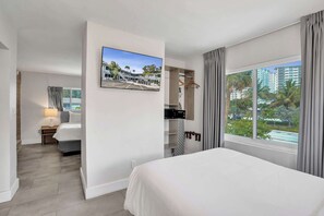 Ein Hotelzimmer mit Bett, Wandfernseher, einem Fenster mit Vorhängen und Blick ins Freie.