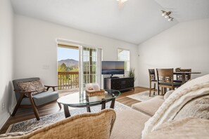 A spacious living room with a glass coffee table, a television, and a dining area with chairs. - Apple Orchard 2BR | Views | EVCharger (Banner Elk)