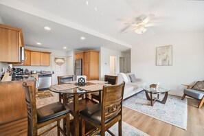 A modern kitchen with wooden cabinets, a dining area with a glass table, and a ceiling fan. - Apple Orchard 2BR | Views | EVCharger (Banner Elk)