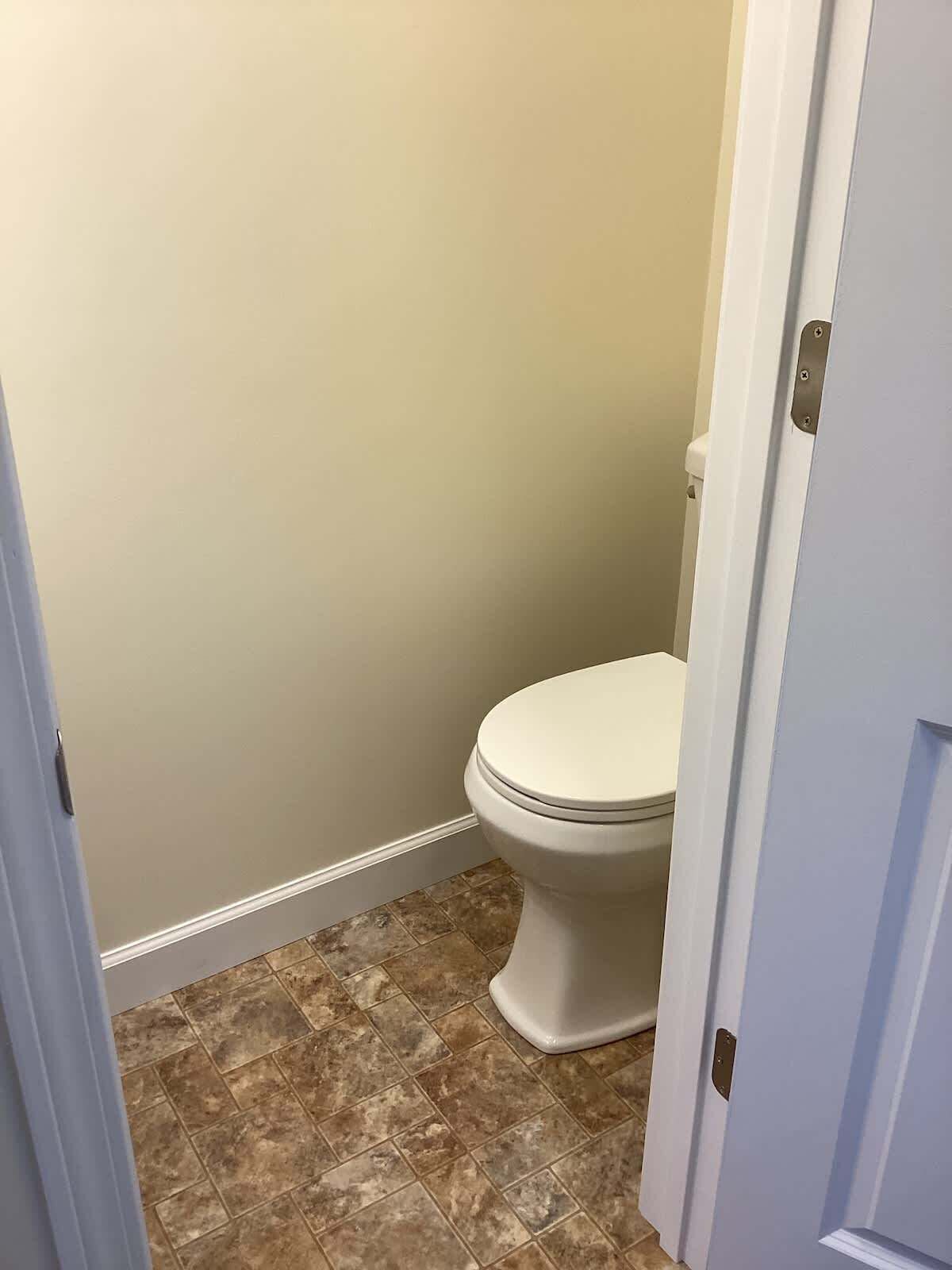 Ein Badezimmer mit Toilette, beige Wänden und braunen Fliesen.