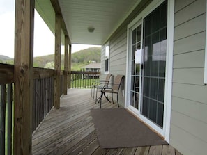 A covered porch with a wooden deck, a sliding glass door, and two chairs.