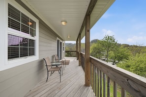 A covered porch with a wooden railing, two chairs, and a table.