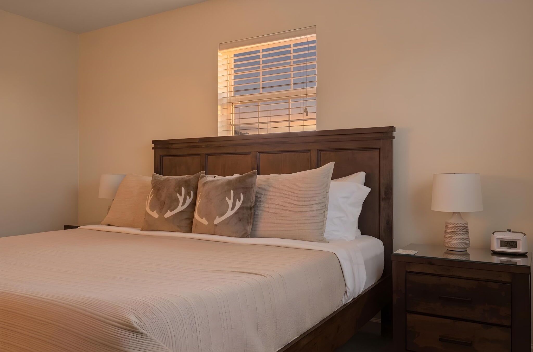 A neatly made bed with a headboard, a bedside lamp, and a nightstand with a clock.