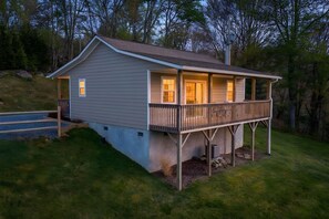 A single-story house with a porch and a small deck, surrounded by trees.