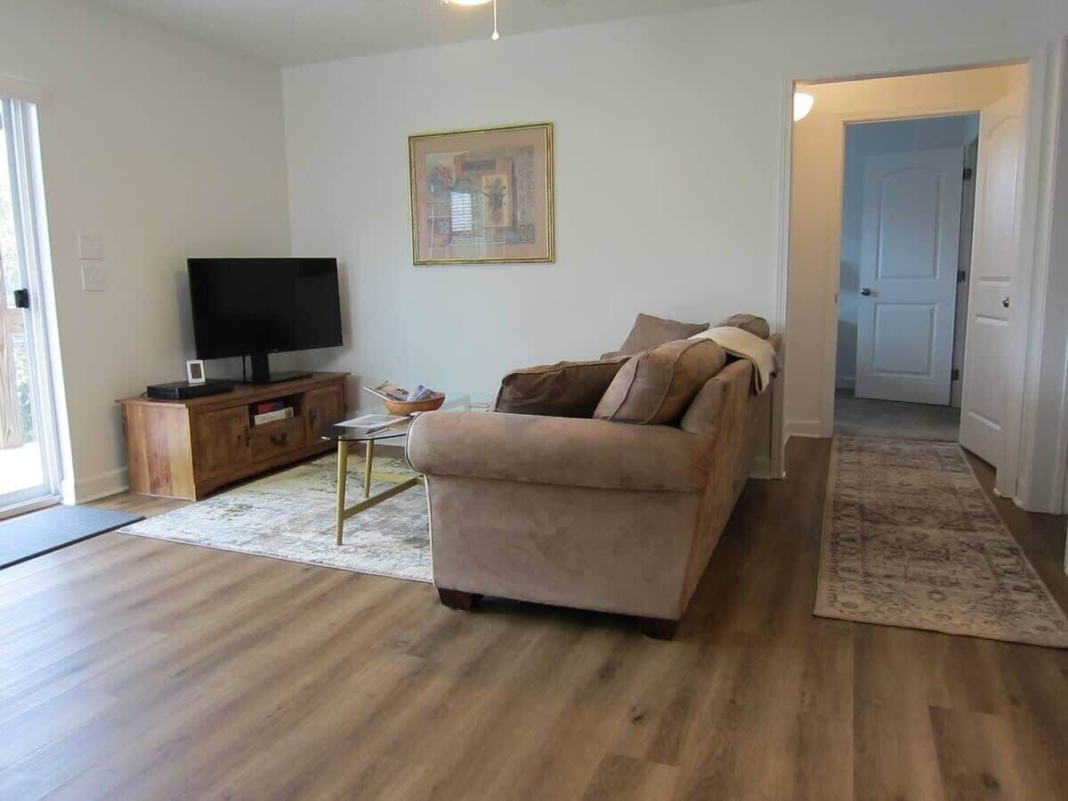 A living room with a sofa, a TV on a wooden cabinet, a rug, and a door leading to another room.