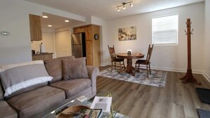 A living room with a sofa, a dining table with chairs, a coat rack, and a kitchen area with wooden cabinets and a refrigerator. - Amazing View, EV Charger, Walk to Banner Elk (Banner Elk)