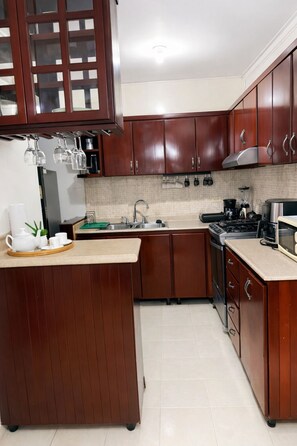 A kitchen with wooden cabinets, a sink, a stove, and a microwave. - Cozy Apt | WiFi +AC | Great Location| Easy Checkin (Santo Domingo)