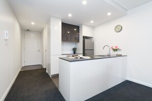 A modern kitchen with white cabinetry, a built-in island with a sink, a clock on the wall, and a door leading to another room. - Elevated Stay with Refined Interiors and Courtyard (Barton)