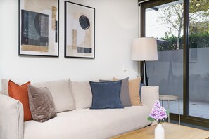 A living room with a beige sofa, a round table, a lamp, and two framed abstract artworks on the wall. - Elevated Stay with Refined Interiors and Courtyard (Barton)