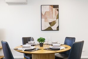 A dining area with a round table, four chairs, and a framed abstract painting on the wall. - Elevated Stay with Refined Interiors and Courtyard (Barton)