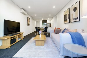 A modern living room with a TV, sofa, coffee table, and dining area. - Elevated Stay with Refined Interiors and Courtyard (Barton)