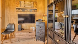 Een kamer met houten lambrisering, een flatscreen televisie, een zwart kastje met lades en een zwarte stoel.