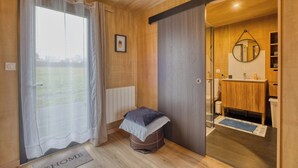 Een kamer met een schuifdeur naar een badkamer, een klein krukje met kussens, een ingelijst schilderij aan de muur, en een deurmat waarop 'HOME' staat.