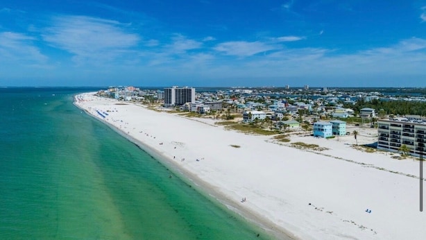 Paisagem costeira com uma extensa praia de areia, edifícios e céu azul límpido.