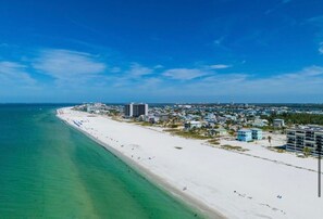 Paisagem costeira com uma extensa praia de areia, edifícios e céu azul límpido.