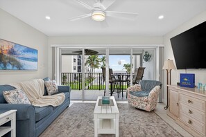 A living room with a sofa, armchair, coffee table, TV, and a balcony with outdoor furniture. - 
NEW Gulf‑Front 2BR-2BA - Direct View of Pool-Beach-Gulf (Fort Myers Beach)