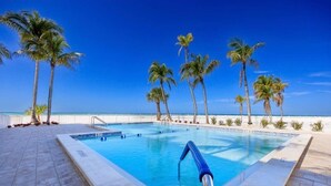 Uma piscina com água azul cristalina, cercada por palmeiras e vista para o oceano.