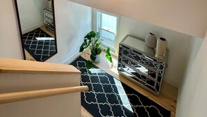 A modern room with a black and white patterned carpet, a wooden staircase, a mirror, a window with a view, and a small plant. - Charming 3-bedroom beach cottage in beautiful Fairfield with AC (Fairfield)