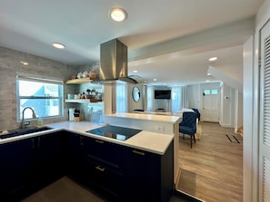 Een moderne keuken met een centraal eiland, inbouwapparatuur en een eethoek met een blauwe beklede stoel.